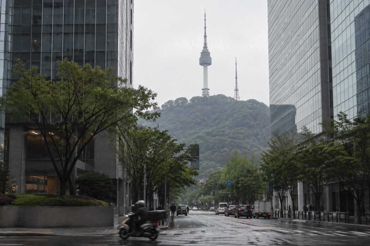The tower on Namsan rising above the tree-covered summit, seen from a city street below
