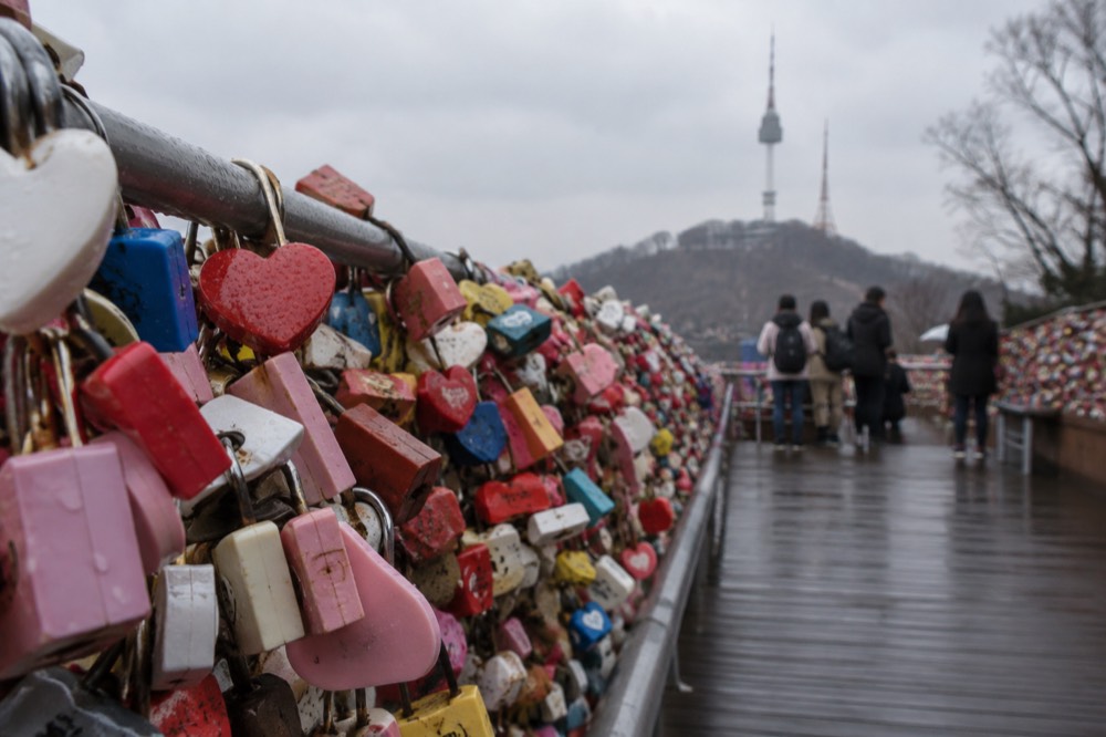 A single heart-shaped padlock hanging among hundreds of locks on a terrace railing