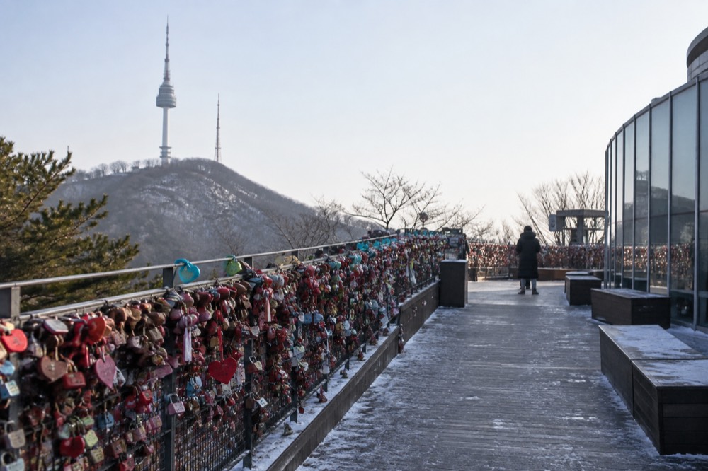 Hundreds of padlocks clipped to wire mesh fencing along an open terrace walkway