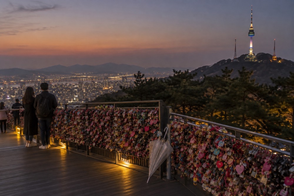 A hilltop terrace at dusk with padlock fences in the foreground and a lit tower rising above
