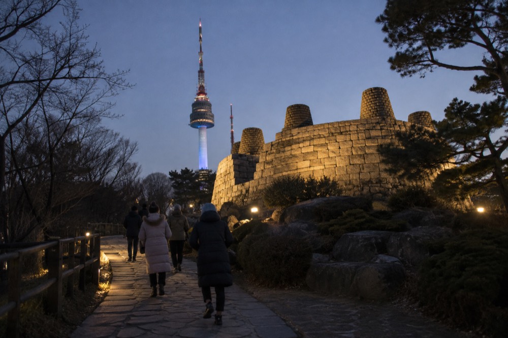 Evening walking group on a lit stone path near a lit tower on a Seoul summit
