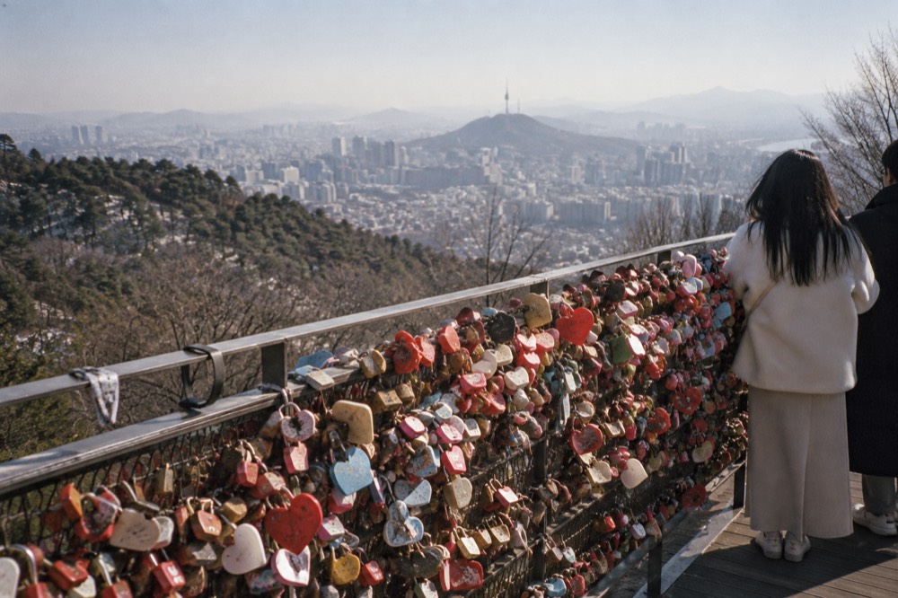 Padlocks attached to railings on an open summit terrace with city towers behind
