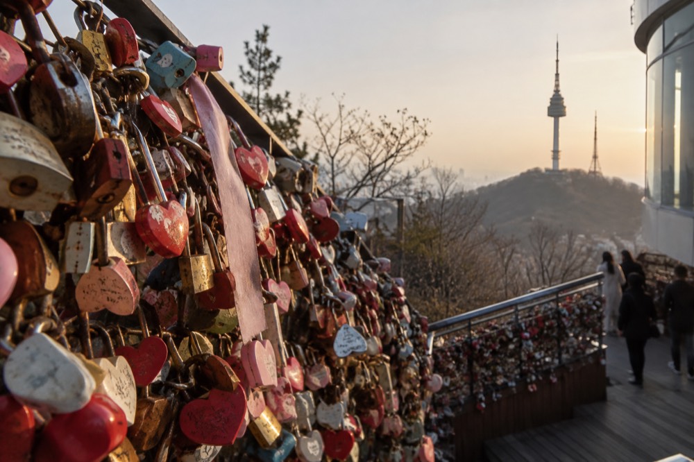 Close-up of hundreds of padlocks attached to the love lock railings with N Seoul Tower in soft focus behind