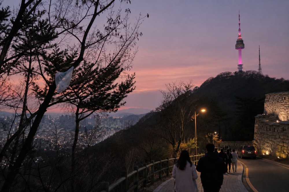 N Seoul Tower lit up at dusk above the forested summit of Namsan