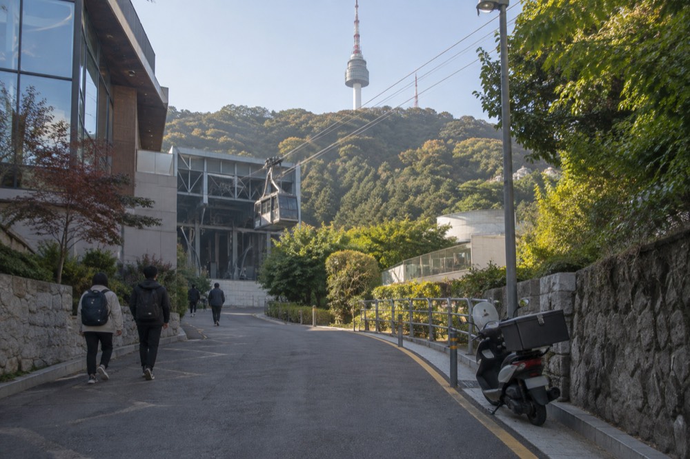 Paved uphill street leading from Myeongdong toward the cable car station with the Namsan hillside above
