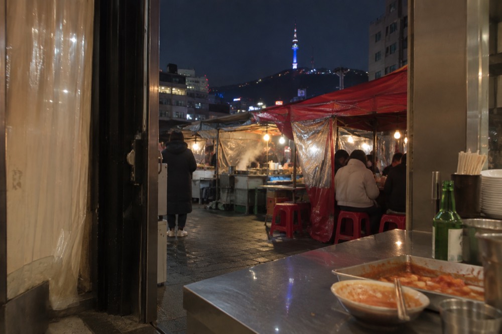 Myeongdong street food stalls and shop lights at night with the illuminated tower on the hillside behind