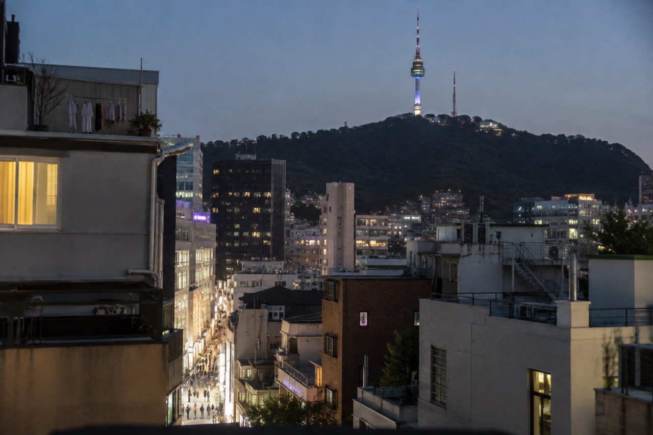 Evening view across Myeongdong rooftops toward the lit N Seoul Tower on the forested Namsan hillside
