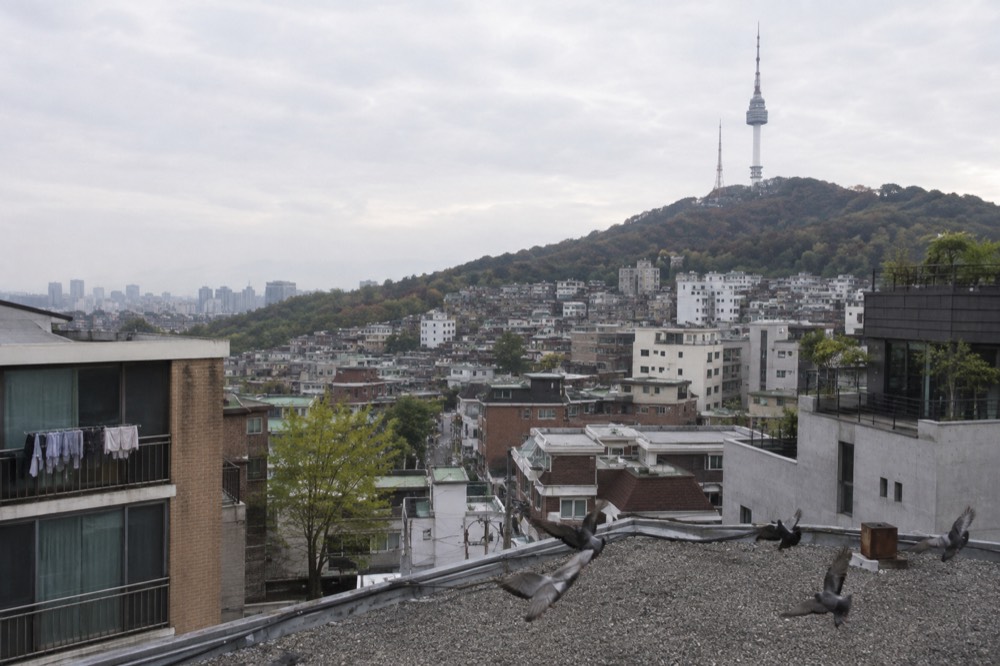 View across Seoul rooftops toward a tall tower on a forested hill in the city centre