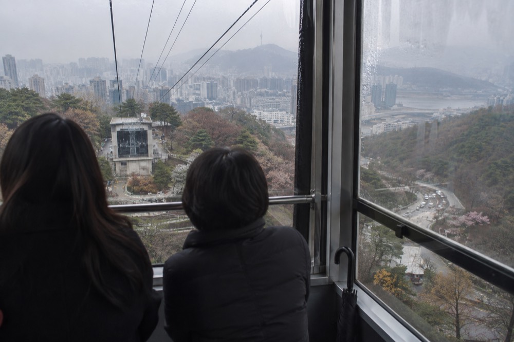 Glass-walled cable car cabin interior with Seoul skyline visible through the windows
