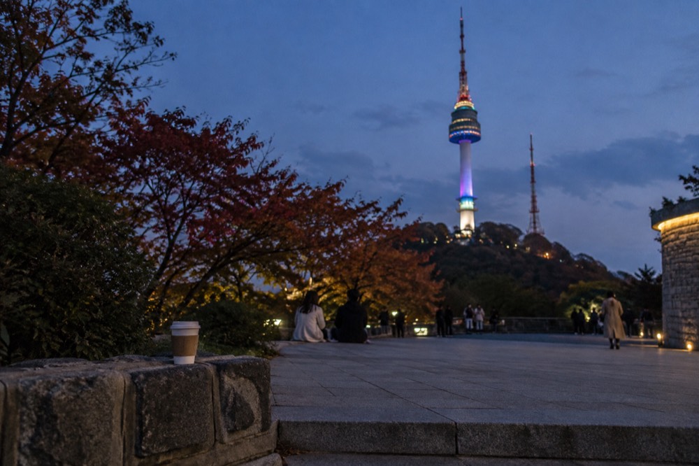 N Seoul Tower glowing with coloured lights against a dark evening sky above Seoul