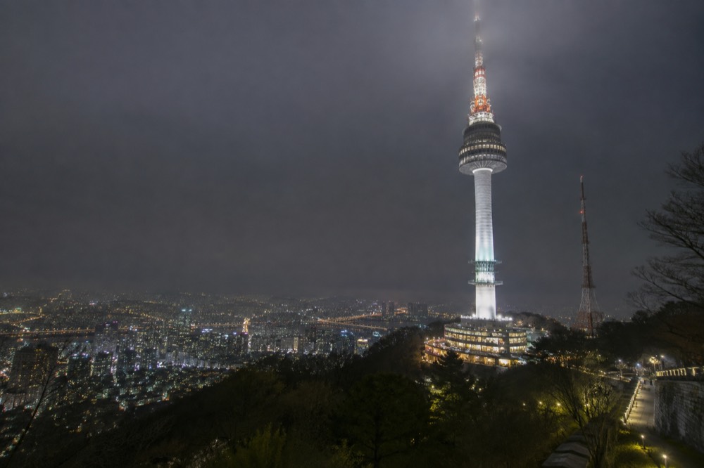 Close view of the N Seoul Tower mast lit up at night above the city lights of Seoul