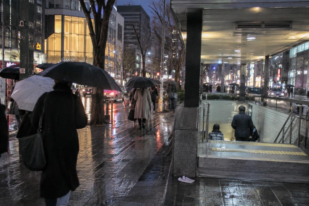 Umbrellas on a wet Seoul street with neon signs reflecting in puddles