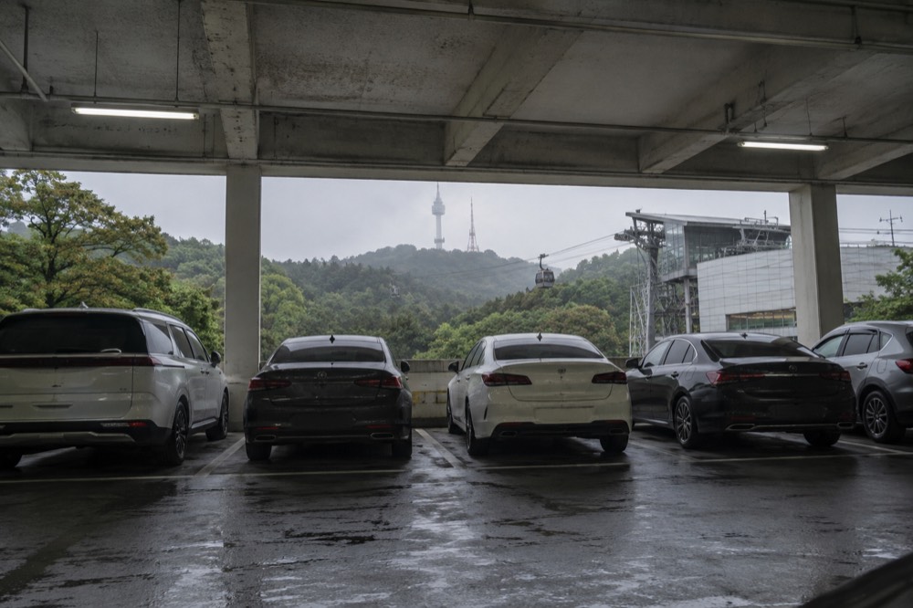 Rows of parked cars in a multi-storey car park at the base of a forested hill