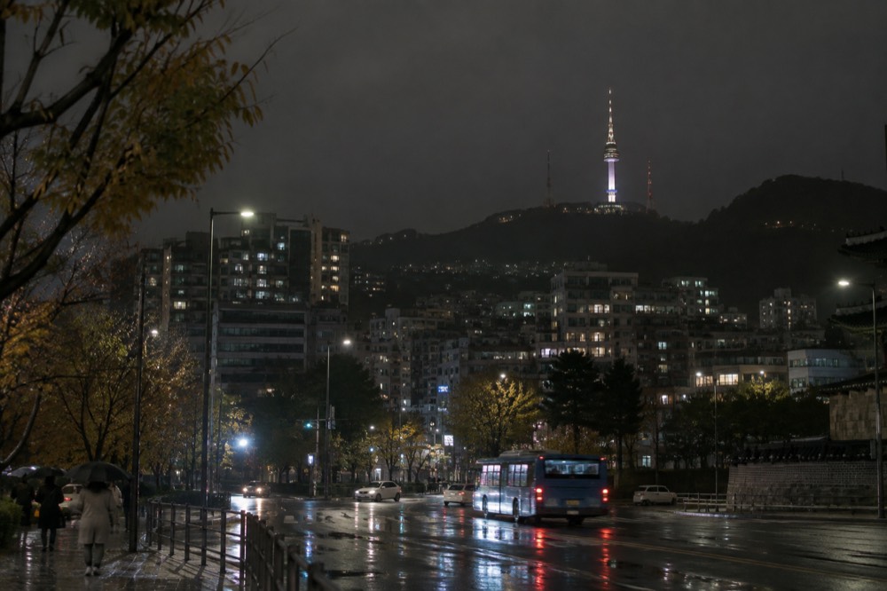 The lit tower seen from a distance across the night city, a bright column above the skyline