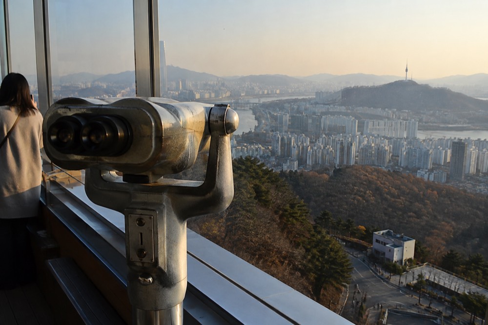 A viewing telescope mounted at a window overlooking a sprawling city