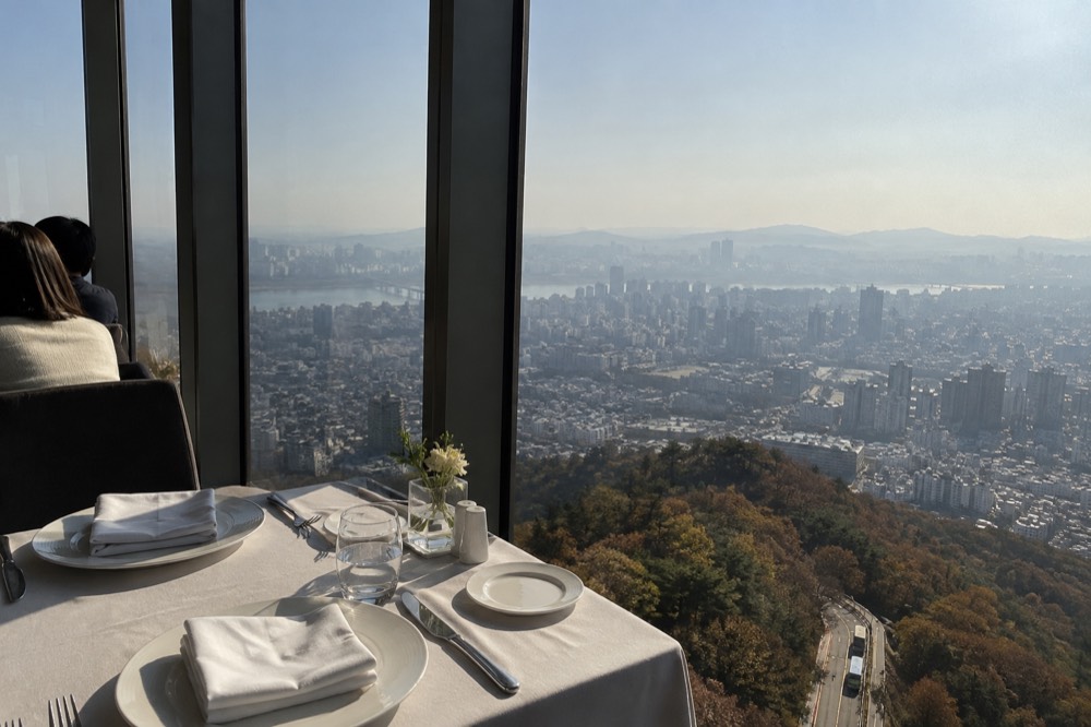 A dining table beside the window at a tower restaurant with the Seoul cityscape spread below