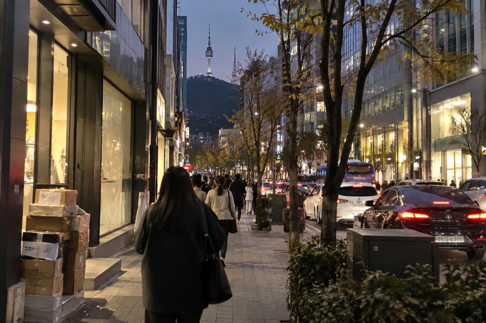 Evening street scene in Myeongdong with shopfronts lit and the hillside rising behind
