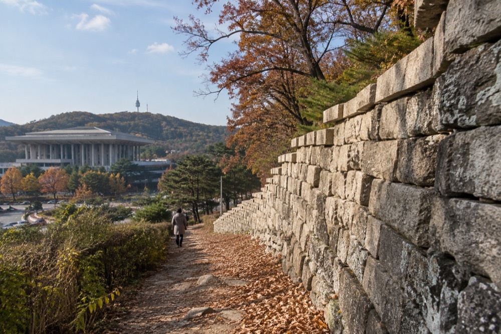 An old stone city wall running along a forested ridge above Seoul
