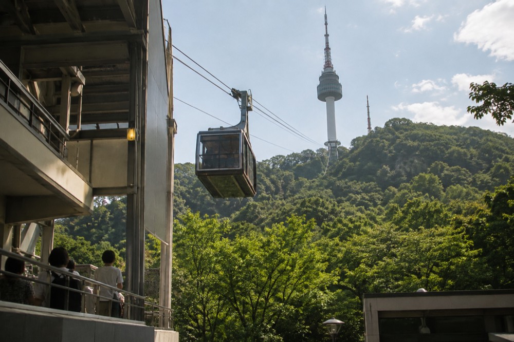 A cable car cabin ascending above a forested hill toward a tower
