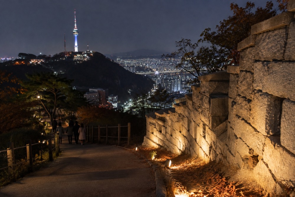 Old stone fortress wall lit softly at night above a glowing city district