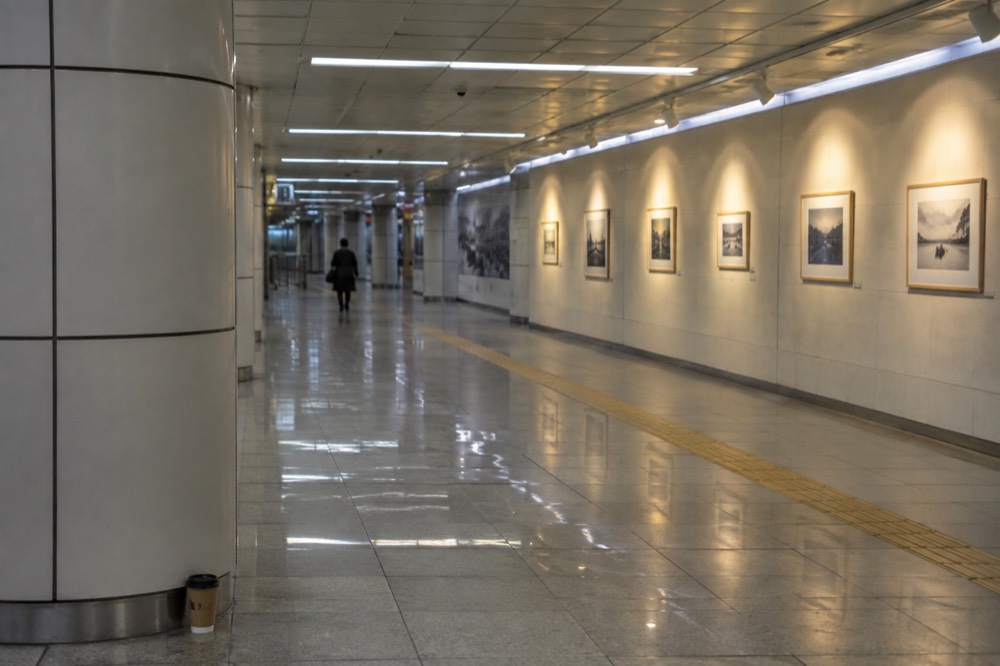 Long modern underground gallery passage with soft lighting and art displays along the walls