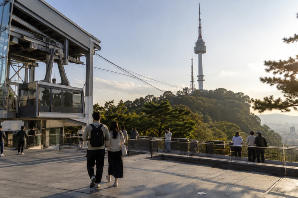 Namsan summit plaza with the tower rising above trees and a city panorama beyond