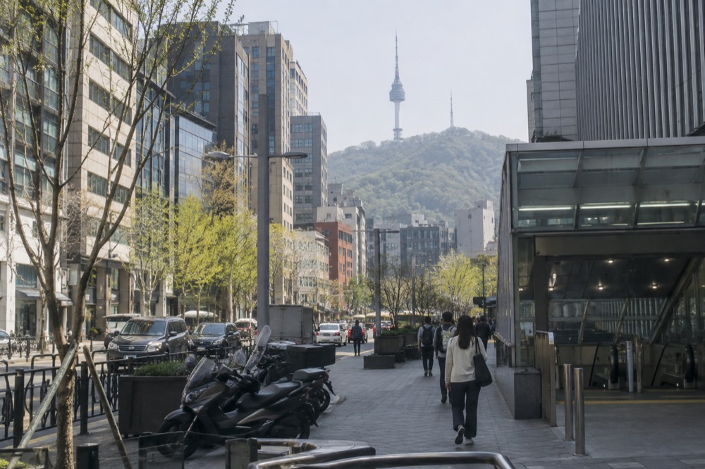 Hotel buildings of different heights along a city street with a wooded mountain rising behind them