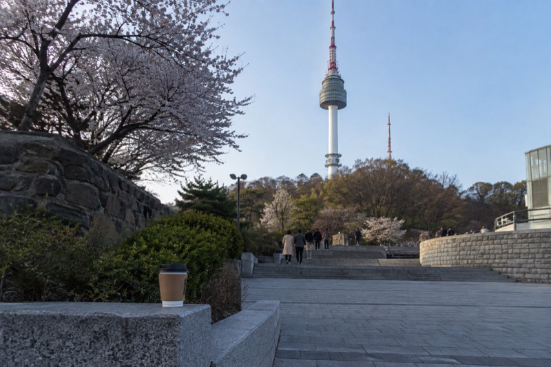 An open paved plaza and terraces around the base of a tall tower, with visitors walking freely.