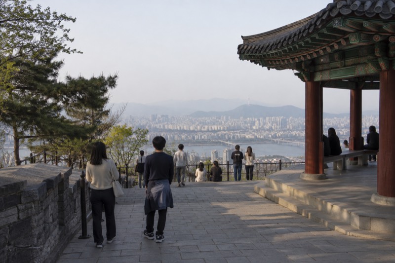 Visitors standing on an open summit terrace, looking out over a sprawling city in daylight.